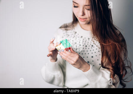 UFA, Russland - Januar 14, 2018: Eine attraktive brünette Frau mit langem Haar löst ein Puzzle, eine zweiseitige Rubik's Cube auf einem weißen Hintergrund. Fokus auf Stockfoto