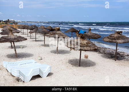 Windiges Wetter auf Meer, Liegen sind auf leeren Sandstrand mit Sonnenschirmen aus Palmenblättern gefaltet. Die Tunesien, Afrika im Mai Stockfoto