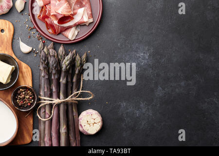 Bündel von frischem violette Spargel Kochen mit Speck, Knoblauch und Gewürzen auf rostigen strukturierten Hintergrund Stockfoto