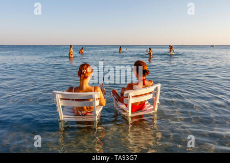 Zwei Frauen sitzen auf Sesseln im Wasser, Strand in Cesme, Izmir, Türkei Stockfoto