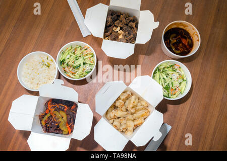 Blick von oben auf die Chinesischen take away mit Stöcken auf Holztisch hacken. Pikante asiatische Lebensmittel in White Box - Salat, souse, Reis mit Ei, chemische Rindfleisch, knackige Ch Stockfoto