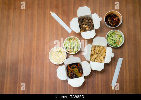 Blick von oben auf die Chinesischen take away mit Stöcken auf Holztisch hacken. Pikante asiatische Lebensmittel in White Box - Salat, souse, Reis mit Ei, chemische Rindfleisch, knackige Ch Stockfoto