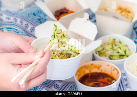 Essen chinesisch Take Away mit Stöcken zu Hause mit Bettwäsche im Hintergrund hacken. Pikante asiatische Lebensmittel in White Box - Salat, souse, Reis mit Ei, Stockfoto