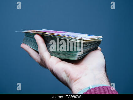 Mann Hand bietet Stapel Stapel Euro Dollar Währung tausende von Banknoten gegen grauer Hintergrund Stockfoto