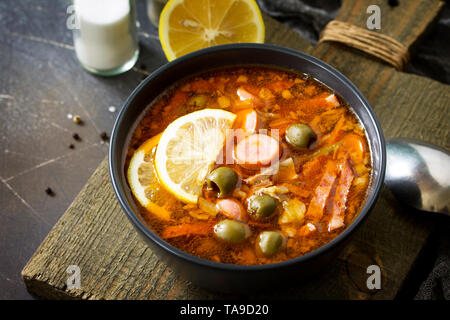 Traditionelle russische Suppe Solyanka mit Fleisch, Wurst, Gemüse, Kapern, Essiggurken und Oliven mit Zitrone auf schwarzem Hintergrund. Im rustikalen Stil. Stockfoto