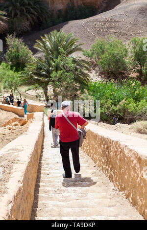 TOZEUR, TUNESIEN - ca. Mai, 2012: Touristen nach unten auf der Treppe zum Zeichen verlegt am Hang mit Steinen und Kies. Bienvenue Chebika, Willkommen inscriptio Stockfoto