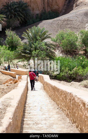 TOZEUR, TUNESIEN - ca. Mai, 2012: Touristen nach unten auf der Treppe zum Zeichen verlegt am Hang mit Steinen und Kies. Bienvenue Chebika, Willkommen inscriptio Stockfoto