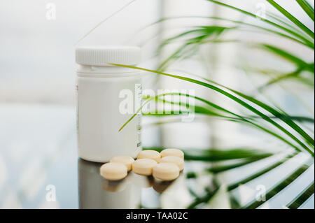 Plastikflasche mit Streulicht Pillen auf einem Glastisch, auf einem natürlichen Hintergrund und auf einem Hintergrund von grünen Blättern. Stockfoto