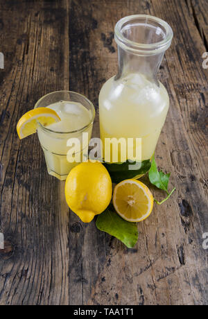 Frische organische Limonade in ein Glas mit Zitronen und Blätter und ein Glas Limonade auf einem rustikalen Holztisch von Oben nach Unten anzeigen Stockfoto