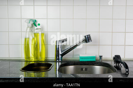 Küche Waschbecken und Wasserhahn mit einem Schwamm und Bürste auf schwarzem Granit Tisch und gelbe Küche sauberer und Spülmittel hinter Stockfoto