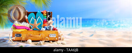 Volle Koffer mit Zubehör am tropischen Strand Stockfoto