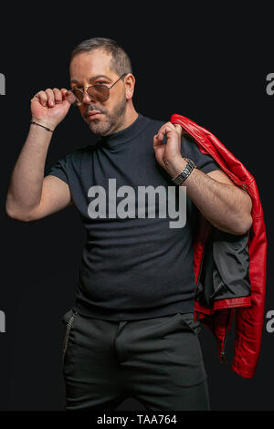 Ein Mann mit Sonnenbrille vor einem schwarzen Hintergrund blickt ernst in die Kamera Stockfoto