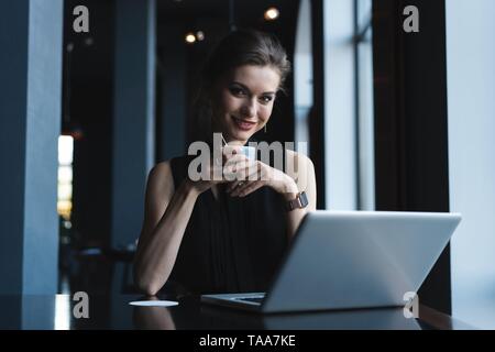 Bei der Arbeit konzentriert. Selbstbewussten jungen Frau in Smart Casual Wear Arbeiten am Laptop, während in der Nähe der Fenster in kreative Büro oder Cafe sitzen. Stockfoto