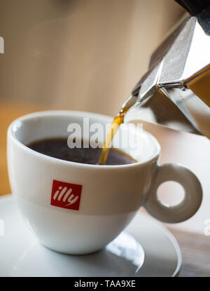 Kaffee wird von bialetti Kaffeemaschine in Illy Cups mit bokeh Hintergrund gegossen Stockfoto
