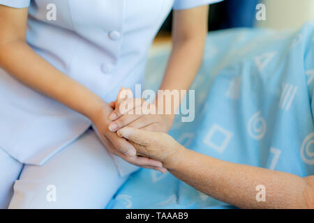 Krankenschwester sitzen auf einem Krankenhausbett neben eine ältere Frau helfende Hände, die Altenpflege Konzept Stockfoto