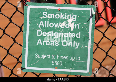 Ein grünes Schild ist auf einem Maschendrahtzaun auf einem Spielplatz gehangen, und sagt "Rauchen ist nur in den gekennzeichneten Bereichen erlaubt, $ 500 fein'. Stockfoto