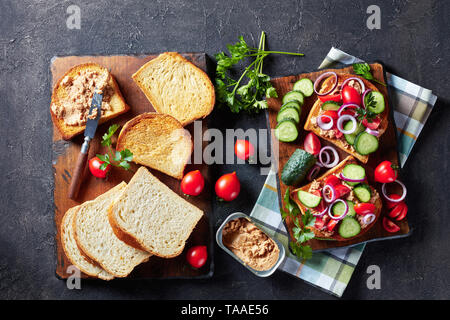 Cod Leber Creme auf Toast mit Gurken, Tomaten und roter Zwiebel Ringe auf einem Schneidebrett mit Brot aus Weizen und Zutaten, Ansicht von oben, flatlay Stockfoto