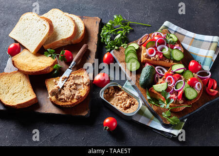 In der Nähe von Toast mit Lebertran Pastete, mit geschnittenen Gurken, Tomaten und roter Zwiebel Ringe auf einem Schneidebrett mit Zutaten aus einer Küche Register abgerundet Stockfoto