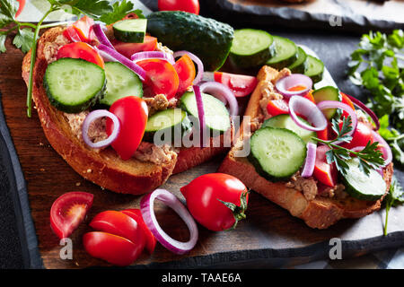 Sandwiches mit Lebertran Pastete, mit geschnittenen Gurken, Tomaten und roter Zwiebel Ringe auf einem Schneidebrett mit Zutaten auf einem Küchentisch überstieg, Stockfoto