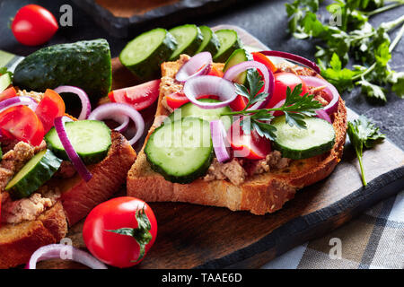 In der Nähe von Sandwiches mit Lebertran Pastete, mit geschnittenen Gurken, Tomaten und roter Zwiebel Ringe auf einem Schneidebrett mit Zutaten aus einem Ki aufgefüllt Stockfoto