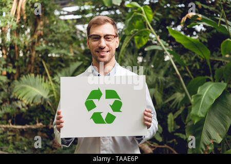 Lächelnd stattlichen Wissenschaftler im weißen Kittel und Brille holding Karte mit Green recycling Anmelden Orangerie Stockfoto