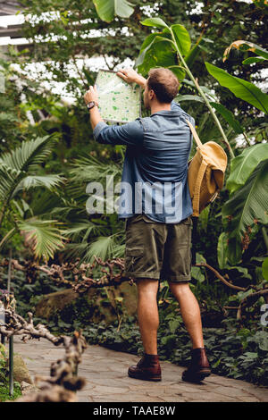 Rückansicht des Reisenden mit Rucksack, Karte und Wandern im grünen, tropischen Wald Stockfoto