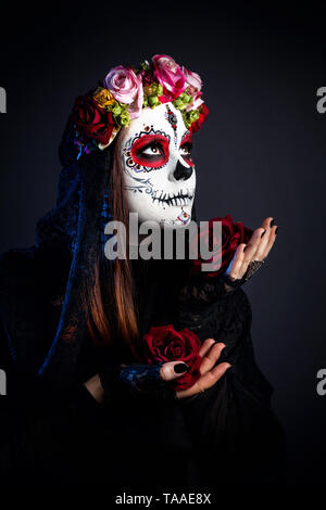 Mädchen mit Sugar Skull mit rosa Blüten feiert Tag der Toten auf schwarzen Hintergrund machen Stockfoto