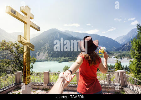 Touristische Frau mit Hut mit einem Mann an der schönen Aussicht auf die Berge See in den Bergen in der Nähe von grossen Goldenen Kreuz in Kasachstan Stockfoto