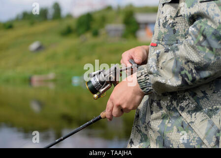 Die Fischer Holding in seinen Händen eine Angelrute und reeling Linie auf der Spule. Die Drehrichtung der Haspel schafft einen verschwommenen Effekt. Stockfoto