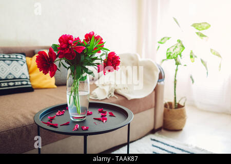 Innenraum der Wohnzimmer mit Pfingstrosen Blumen, Pflanzen und Teppich eingerichtet. Gemütliches Sofa mit Kissen und Tabelle Stockfoto