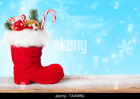 Santa Stiefel mit Süßigkeiten und Geschenke auf einem blauen Hintergrund mit fallenden Schneeflocken Stockfoto