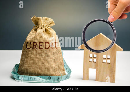 Ein Beutel mit Geld und einem Maßband und das Wort Kredit- und ein Holzhaus. Mangel an Geld, um das Darlehen zu zahlen. Hypothek für den Wohnungsbau. Einsparungen und accumulat Stockfoto