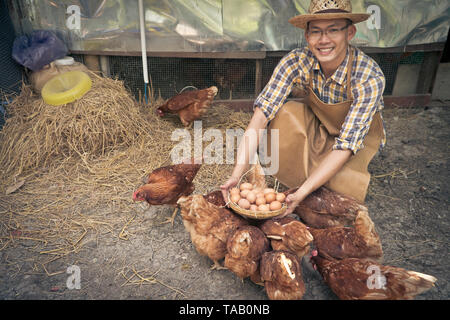 Junge Intelligenter Landwirt wear Plaid Shirt braun Schürze halten Frische Hühnereier in Warenkorb auf einer Hühnerfarm in ihm home Bereich Stockfoto