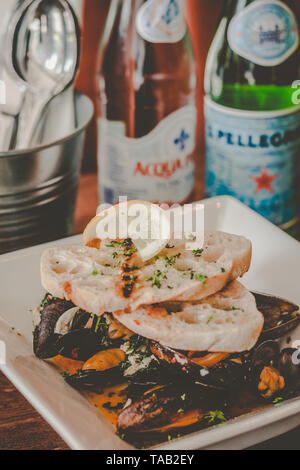 Saute Muscheln in Weißwein und Knoblauch Sauce serviert mit Knoblauch Brot auf der Oberseite Stockfoto