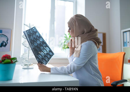 Arzt sitzen. Smart Ärztin tragen weiße Uniform und Kopftuch an einem Tisch sitzen Stockfoto