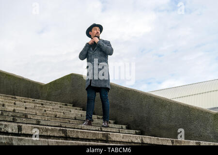 Porträt einer stilvollen hübscher junger Mann mit Mantel im Freien. Ein Mann mit einem Mantel und Schal weg schauen und sich wundern. Stockfoto