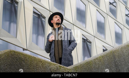 Porträt einer stilvollen hübscher junger Mann mit Mantel im Freien. Ein Mann mit einem Mantel und Schal weg schauen und sich wundern. Stockfoto