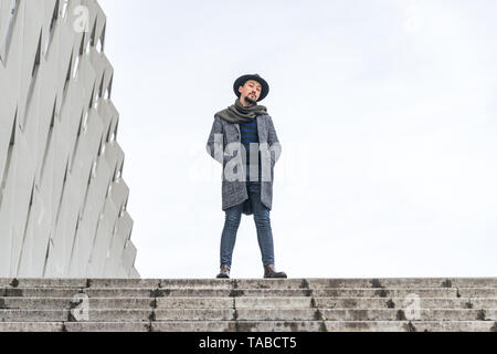 Porträt einer stilvollen hübscher junger Mann mit Mantel im Freien in der Macht stehende darstellen. Ein Mann mit einem Mantel und Schal weg schauen und sich fragen, Stockfoto