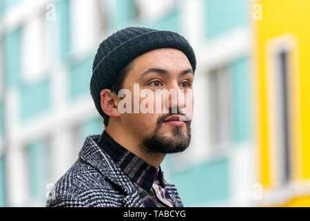 Porträt einer stilvollen hübscher junger Mann mit Mantel im Freien. Ein Mann mit einem Mantel und einem T-Shirt weg schauen und sich wundern. Stockfoto