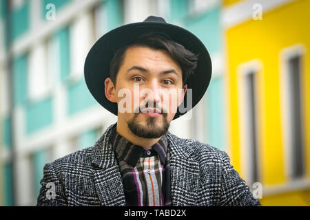 Porträt einer stilvollen hübscher junger Mann mit Mantel im Freien. Ein ernster Mann trug einen Mantel, Hut und Hemd in die Kamera schaut zuversichtlich. Stockfoto