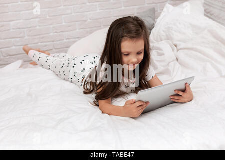 Süßes kleines Kind Mädchen liegt im Bett verwendet digitale Tablet. Kind spielen auf dem Tablet-PC. Stockfoto