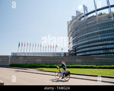 Straßburg, Frankreich, 23. Mai 2019: erwachsene Frau auf Fahrrad mit Hauptsitz des Europäischen Parlaments Gebäude im Hintergrund alle EU-Mitgliedstaaten Fahnen schwenkten Stockfoto