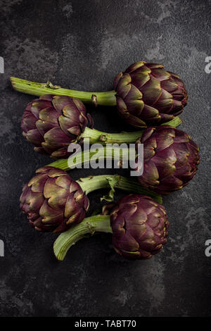 Lila Artischocken blumen Köpfe auf dunklem Schiefer. Stockfoto