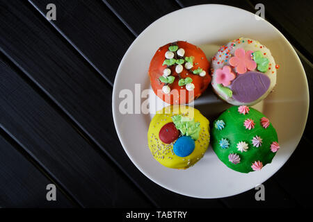 Lecker, bunten Cupcakes - Ostern Kuchen in einer weißen Platte auf einem schwarzen Hintergrund. Hausgemacht. Tageslicht. Ansicht von oben Stockfoto