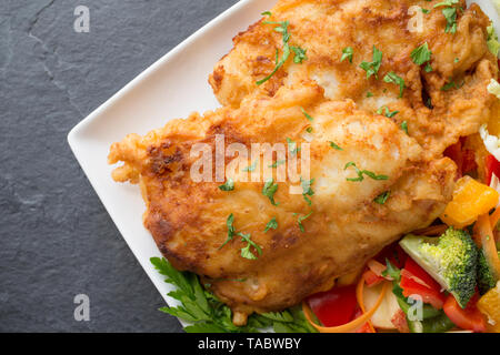 Zwei dicke Filets von Pollack Pollachius pollachius, dass tief in hausgemachter Teig gebraten und serviert mit Obst und rohem Gemüse. Die pollac Stockfoto