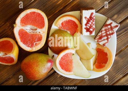 Schwamm Kuchen und Scheiben von Grapefruit und Birnen liegen in einer weißen Platte auf einer hölzernen Oberfläche aus Kiefer Bretter. Frühstücksbuffet im authentischen natürlichen Hotel. Dayli Stockfoto