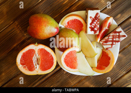 Segmente von Pampelmusen und Grapefruits, Birnen und Kuchen sind in einer weißen Platte auf einem Holztisch aus Kiefer Bretter. Frühstücksbuffet im authentischen natürlichen Hotel. Sommer noch Leben Stockfoto