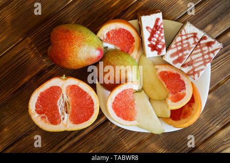 Drei keks Kuchen, Scheiben von Grapefruit und Birnen liegen in einer weißen Platte auf einem Holztisch aus Kiefer Bretter. Frühstücksbuffet im authentischen natürlichen Hotel. Summe Stockfoto