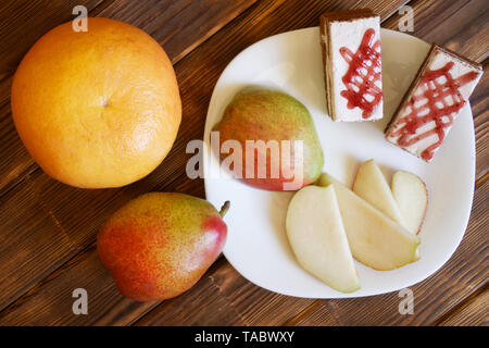 Grapefruit, Kuchen und Scheiben von Birne in eine weiße Platte auf einem Holztisch Kiefer Bretter. Frühstücksbuffet im authentischen natürlichen Hotel. Tageslicht. Stockfoto