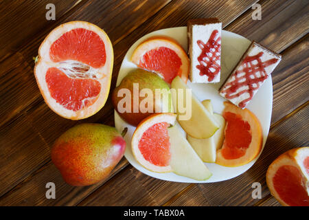 Hausgemachte Kuchen, Scheiben von Grapefruit und Birnen liegen in einer weißen Platte auf einem Holztisch aus Kiefer Bretter. Frühstücksbuffet im authentischen natürlichen Hotel. Sommer s Stockfoto